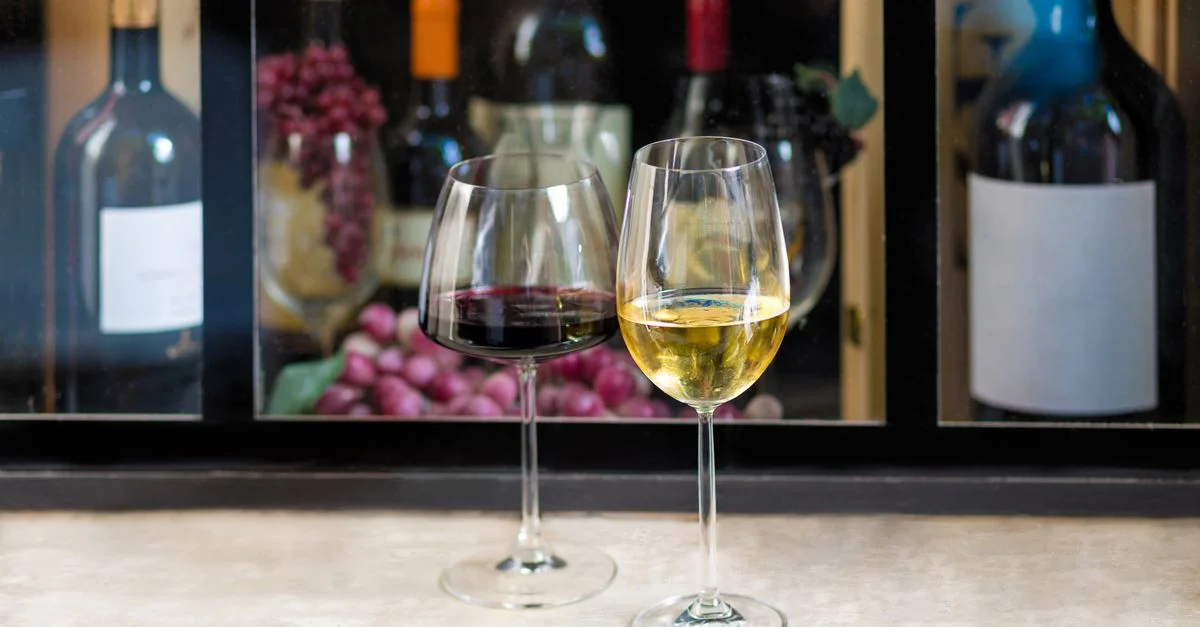 Gros plan sur des verres de vin rouge et blanc avec des bouteilles et des raisins en arrière-plan, parfait pour des thèmes de dégustation de vin.