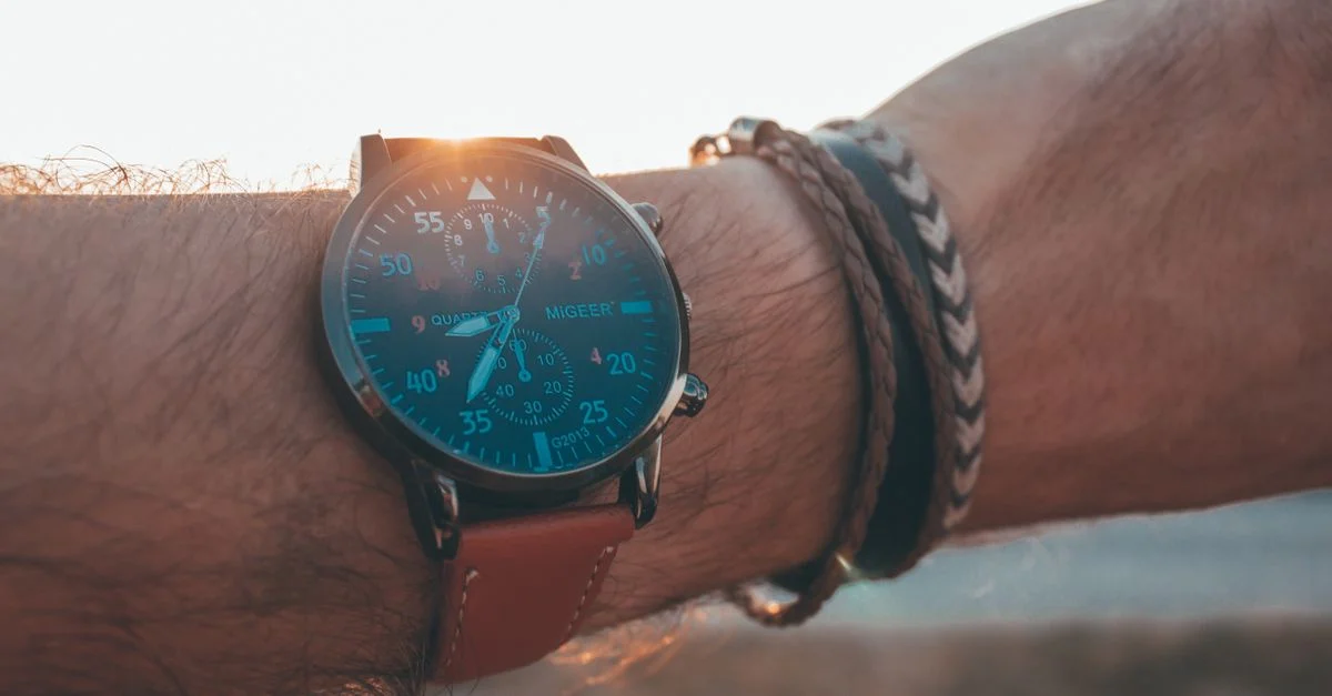 Gros plan sur une montre et des bracelets sur un poignet, avec un fond de coucher de soleil.
