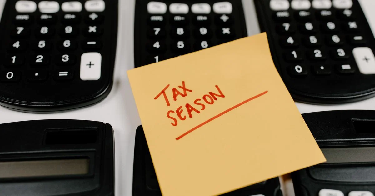 Gros plan sur des calculatrices et une note autocollante étiquetée 'Saison des Impôts', symbolisant la préparation fiscale.