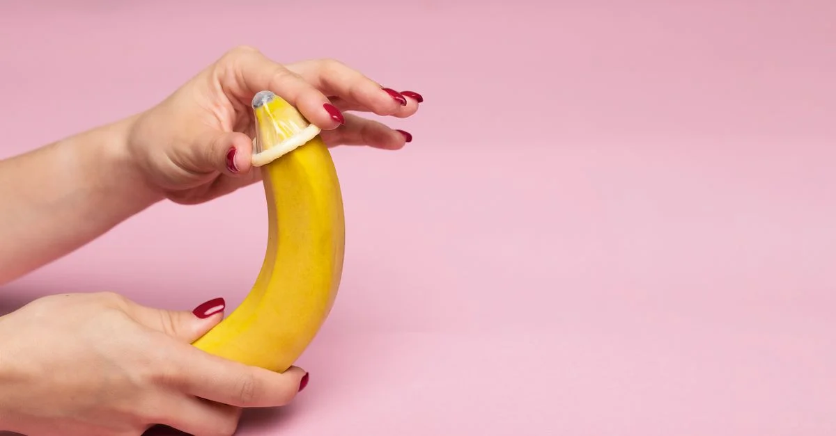 Gros plan sur des mains démontrant l'application d'un préservatif sur une banane, symbolisant l'éducation à la sexualité sécurisée.