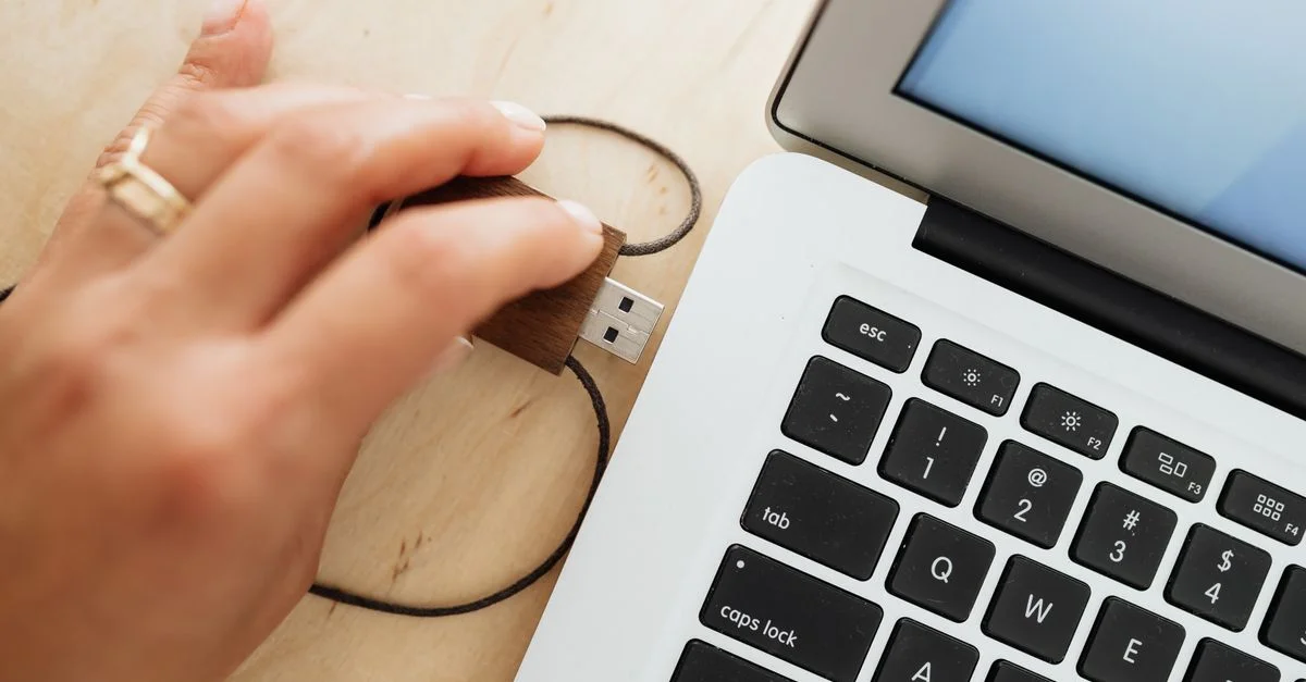 Main insérant une clé USB en bois dans un ordinateur portable sur une table en bois.