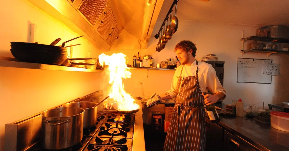 Dans la cuisine animée d'un restaurant, un chef flambe avec dextérité un plat, créant une flamme spectaculaire.
