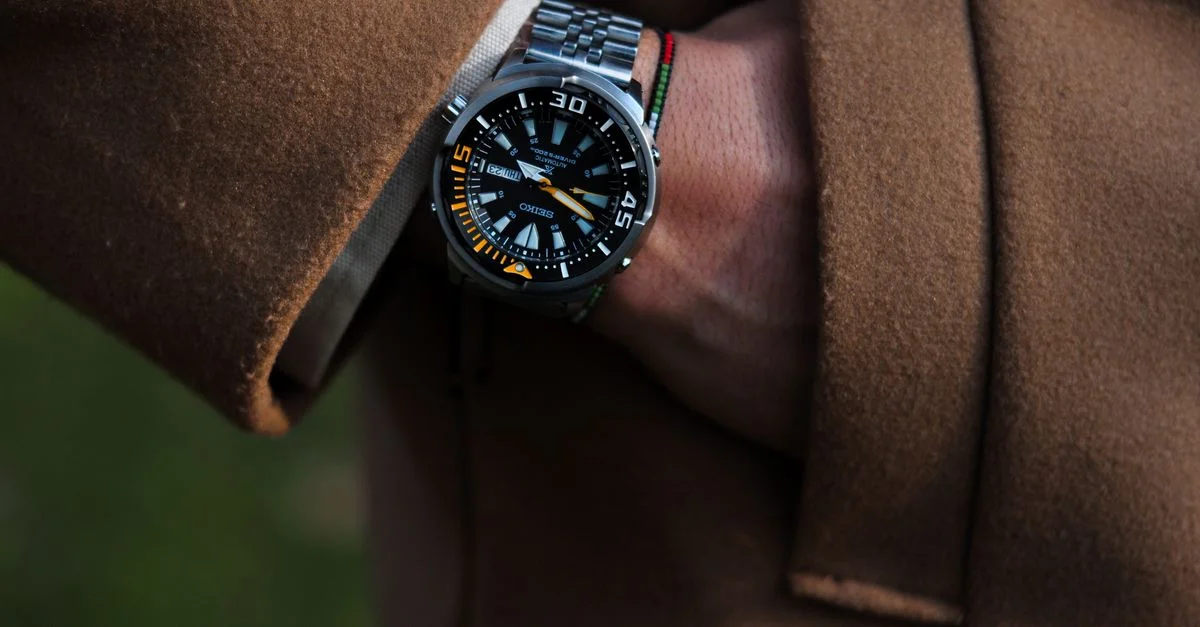 Gros plan d'une montre-bracelet de luxe sur le poignet d'un homme, stylisé avec un manteau marron.