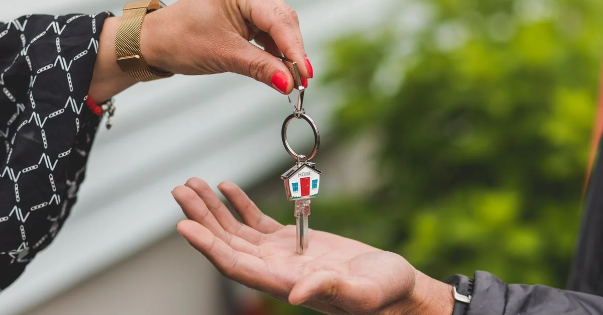 Gros plan d'une main remettant une clé avec un porte-clé en forme de maison, symbolisant une transaction immobilière.