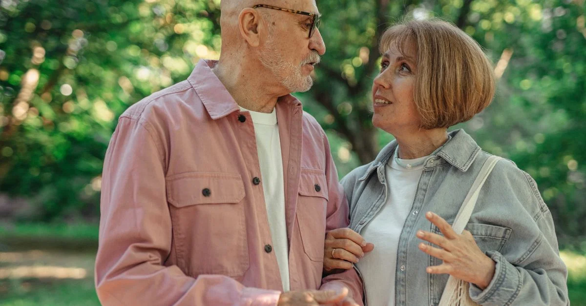 Un couple âgé partage une conversation joyeuse dans un parc verdoyant.