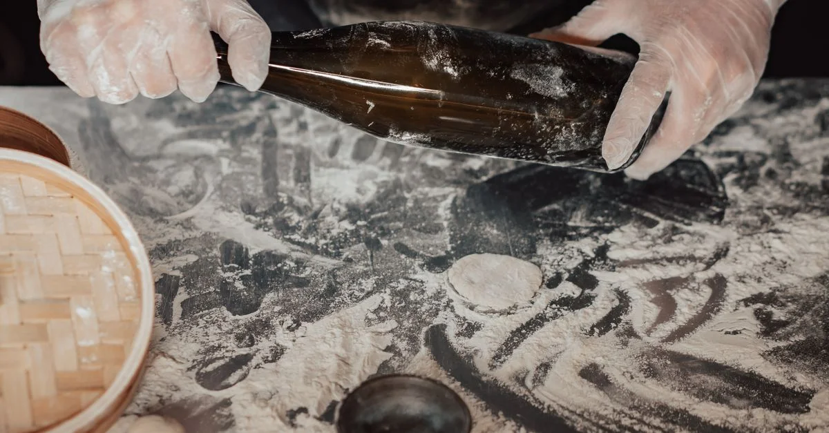 Mains gantées utilisant une bouteille pour façonner la pâte sur une surface de cuisine farinée.